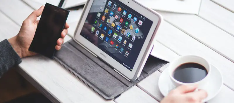 Man holding a smartphone, with a laptop open and a cup of black coffee.
