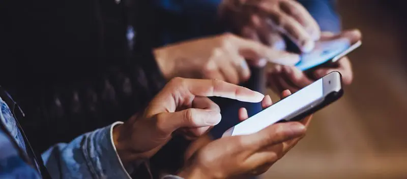 Hands of three people all using smartphones.