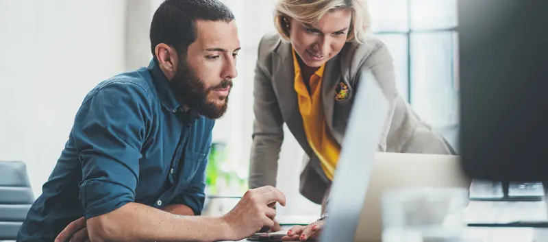 A man and a woman looking at a computer monitor.