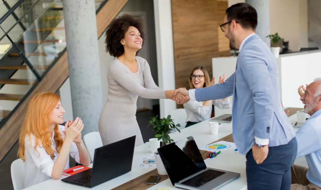 Man and woman shaking hands over a desk.