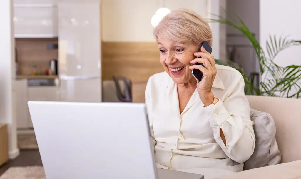 Elderly lady looking at laptop while talking on the phone.