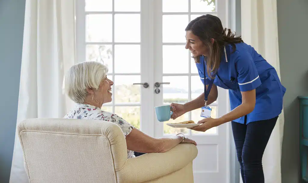 Care home worker serving tea and biscuits to a female care home resident.