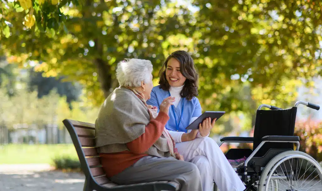 Elderly lasy in a wheelchair and a nurse sitting outside.